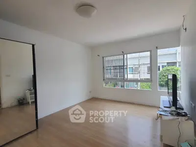 Spacious unfurnished room with large window and wooden flooring, ideal for customization.