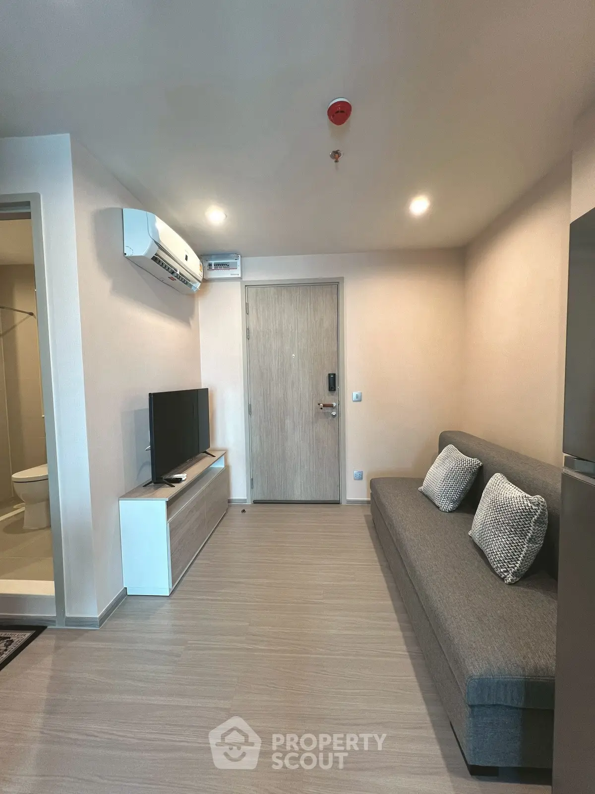 Modern living room with sleek design, featuring a comfortable sofa, wall-mounted TV, and air conditioning.