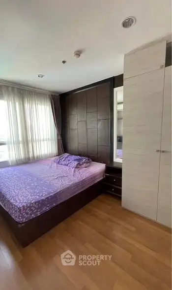 Cozy bedroom with wooden flooring and large window for natural light.