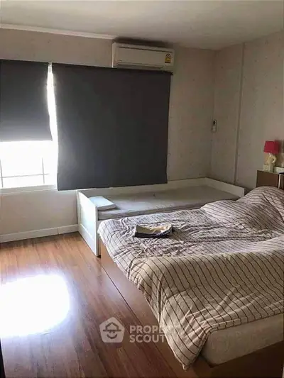 Cozy bedroom with wooden flooring and modern furnishings, featuring a comfortable bed and ample natural light.