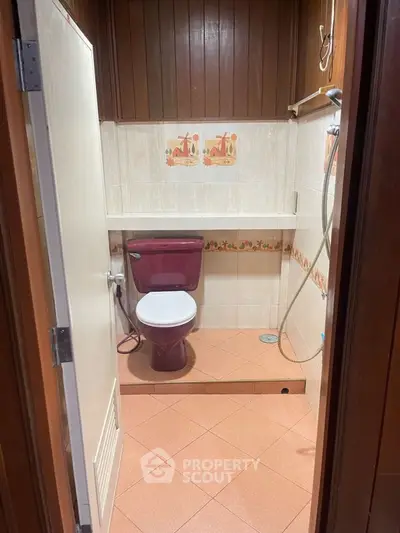 Cozy bathroom with unique maroon fixtures and tiled walls, featuring a shower area and wooden accents.