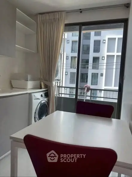 Modern kitchen with washing machine and dining table, featuring large window with urban view.