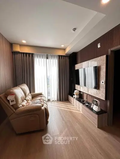 Modern living room with sleek TV setup and cozy seating, featuring floor-to-ceiling windows for natural light.