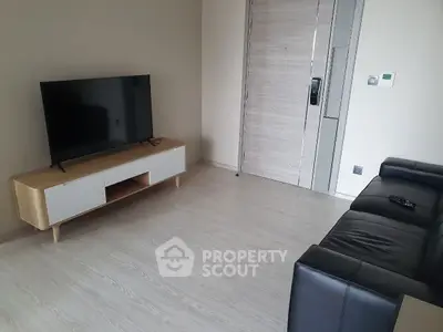 Modern living room with sleek black sofa and flat-screen TV on wooden stand.