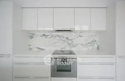 Modern kitchen with sleek white cabinetry and marble backsplash featuring built-in oven.