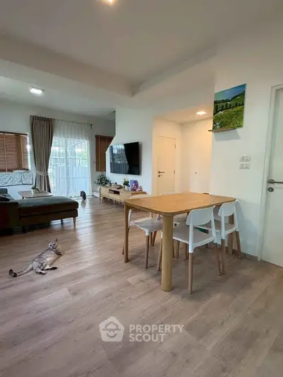 Spacious living room with modern decor and wooden flooring, featuring a cozy dining area and large windows.