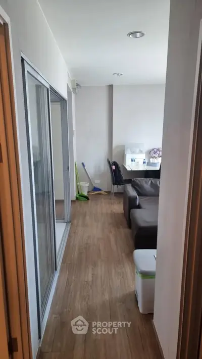 Modern apartment hallway leading to a cozy living room with wooden flooring and sliding glass doors.