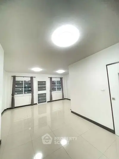 Spacious empty room with glossy tiled floor and large windows, perfect for customization.