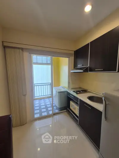 Modern kitchen with sleek cabinetry and balcony access, featuring a washing machine and compact appliances.