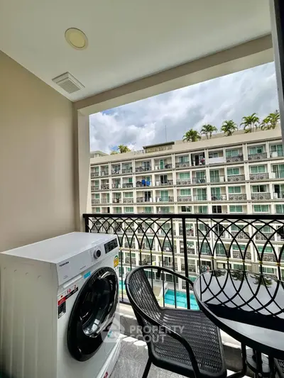 Modern balcony with washing machine and seating, overlooking a stylish apartment complex with pool view.