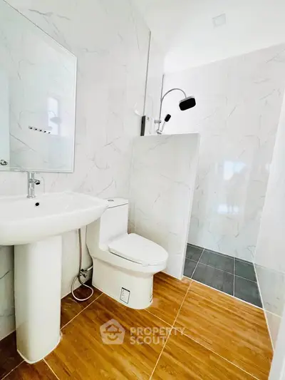Modern bathroom with sleek design, featuring a pedestal sink, toilet, and walk-in shower with elegant tile work.