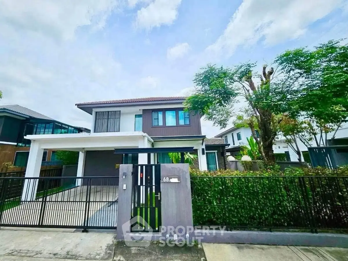 Modern two-story house with gated entrance and lush greenery in a suburban neighborhood.