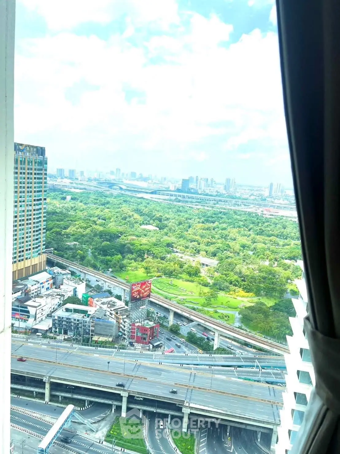Stunning cityscape view from high-rise apartment window overlooking lush greenery and urban skyline.