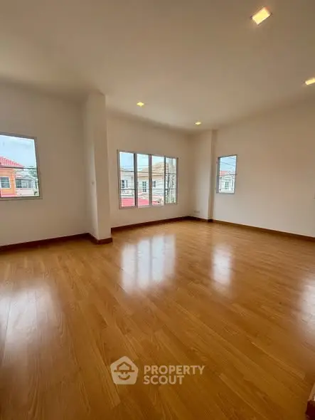 Spacious empty room with wooden flooring and large windows offering natural light.