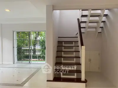 Spacious modern living area with elegant staircase and large windows overlooking greenery.