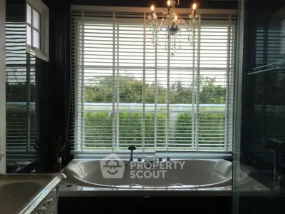 Luxurious bathroom with large bathtub and elegant chandelier overlooking lush greenery.