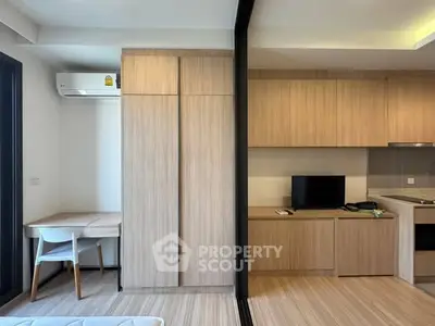 Modern studio apartment with sleek wooden cabinetry and compact workspace.
