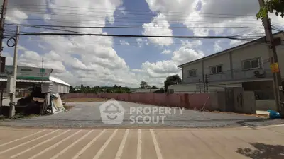 Spacious vacant lot with potential for development, featuring clear skies and adjacent building.