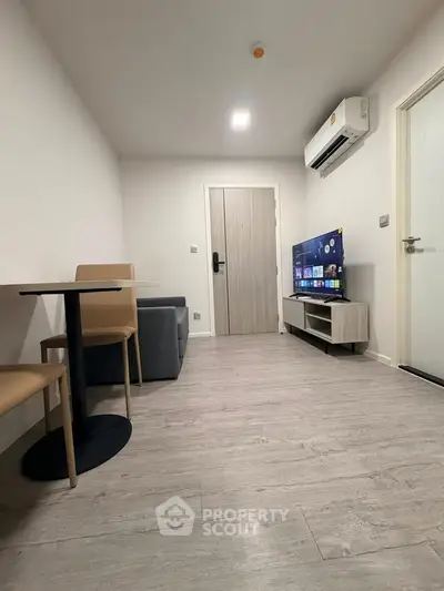 Modern living room with sleek furniture and wall-mounted TV, featuring a minimalist design and air conditioning.
