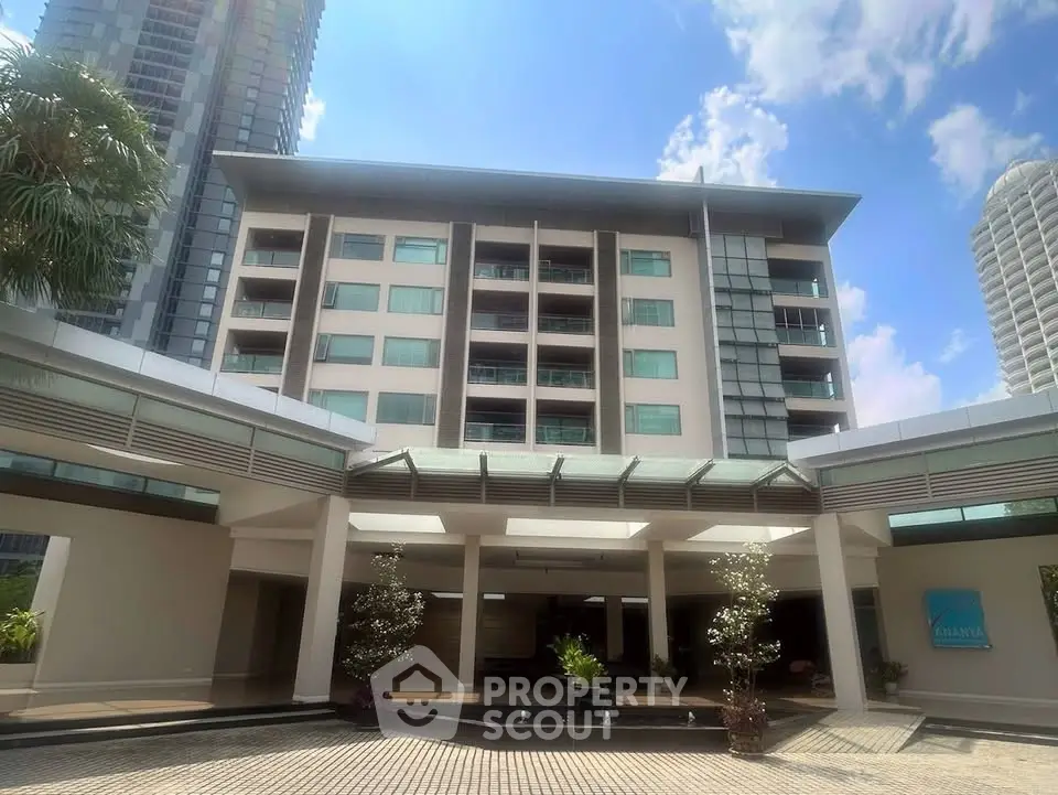 Modern apartment building entrance with glass canopy and lush greenery, showcasing urban living.