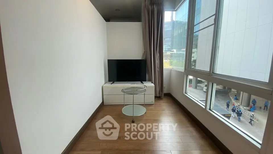 Modern living room with large windows and sleek TV setup in urban apartment.