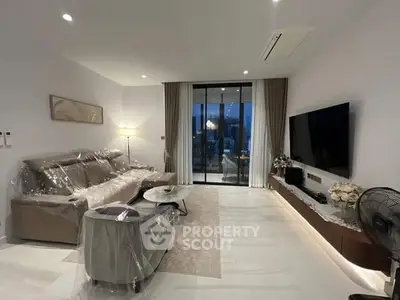 Modern living room with sleek furniture and large TV, featuring a balcony with city view.