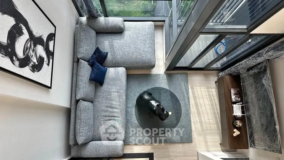 Modern living room with large windows and stylish decor, featuring a cozy gray sofa and abstract art.