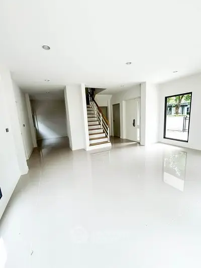 Spacious modern living room with glossy white tiles and staircase in a bright home.