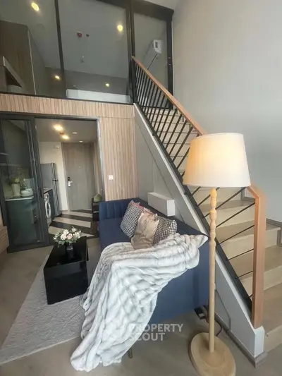 Modern duplex living room with stylish decor and staircase, featuring cozy seating and elegant lighting.