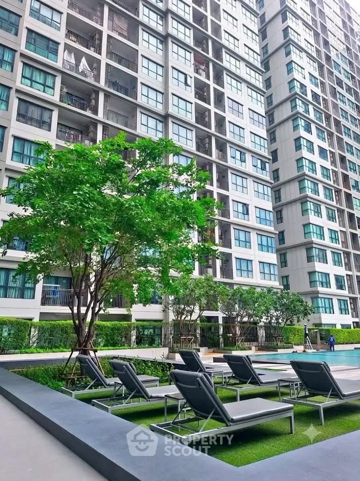 Modern high-rise building with poolside lounge chairs and lush greenery