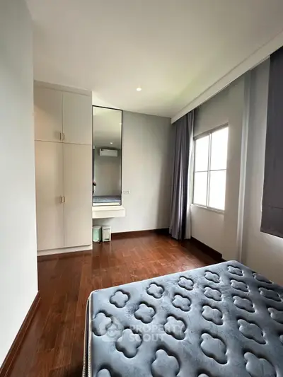 Modern bedroom with hardwood floors and large window, featuring a stylish bed and built-in wardrobe.