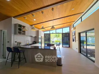 Stunning open-layout kitchen with modern design and pool view, featuring high ceilings and elegant lighting.