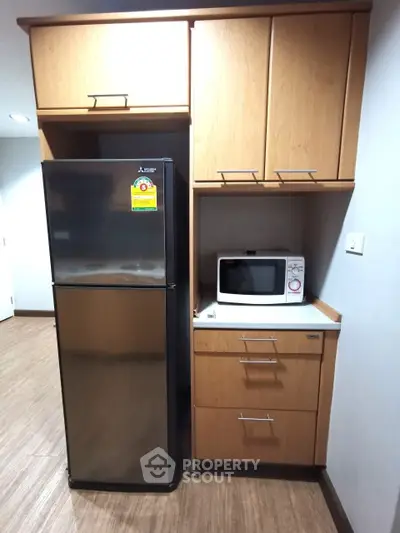 Modern kitchen with sleek fridge and microwave in stylish wooden cabinetry.