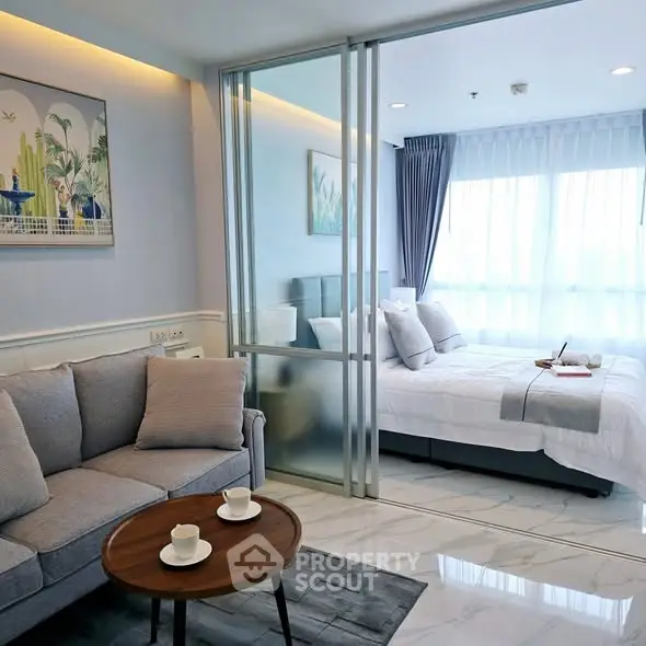 Modern living room with sliding glass doors leading to a cozy bedroom, featuring elegant decor and natural light.