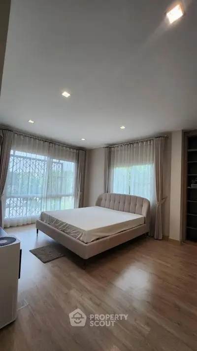Spacious bedroom with large windows and elegant curtains, featuring a modern bed and wooden flooring.