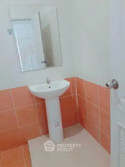 Compact bathroom with pedestal sink and orange tile accents, perfect for modern minimalist design.