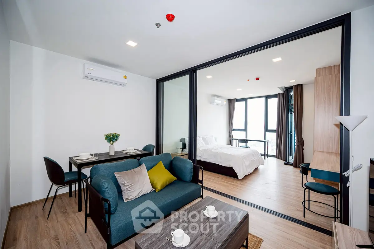 Modern open-plan living room with dining area and bedroom, featuring stylish decor and large windows.