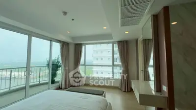 Spacious bedroom with floor-to-ceiling windows and balcony offering stunning city views.