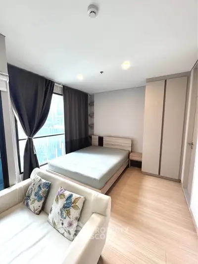 Modern bedroom with large windows and cozy seating area in a stylish apartment.