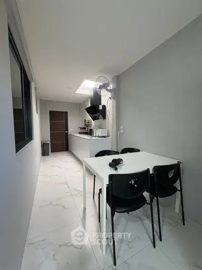 Modern kitchen with sleek white dining table and black chairs, featuring a minimalist design and open layout.
