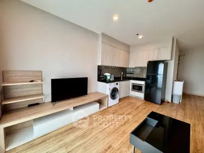 Modern open-plan living room with kitchen, featuring wood flooring and sleek appliances.