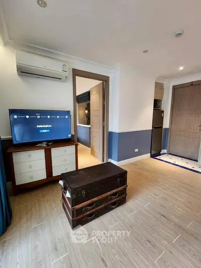Charming living room with modern decor and wooden flooring, featuring a TV and air conditioning.