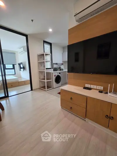 Modern living room with built-in TV unit and adjacent laundry area in stylish apartment.