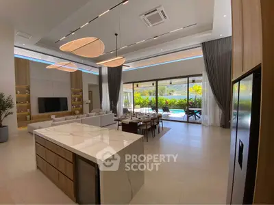 Luxurious open-plan living room with modern kitchen and pool view, featuring high ceilings and elegant lighting.