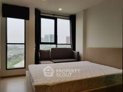 Modern bedroom with large windows offering city views, featuring a cozy bed and stylish sofa.