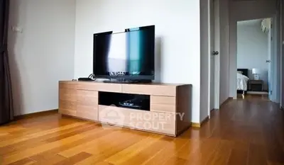 Modern living room with sleek wooden TV stand and flat-screen TV, showcasing minimalist design and warm wooden flooring.