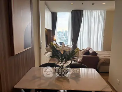 Modern apartment interior with dining area and city view from bedroom window.