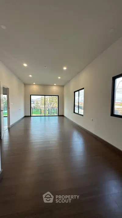 Spacious modern living room with large windows and wooden flooring, offering abundant natural light.