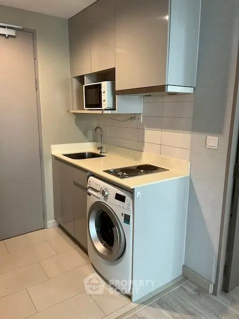 Modern compact kitchen with washing machine and microwave in sleek apartment.