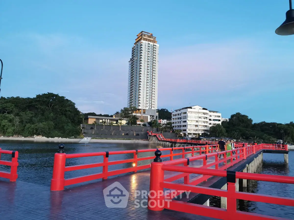 Stunning waterfront view with modern high-rise building and vibrant red bridge at sunset.